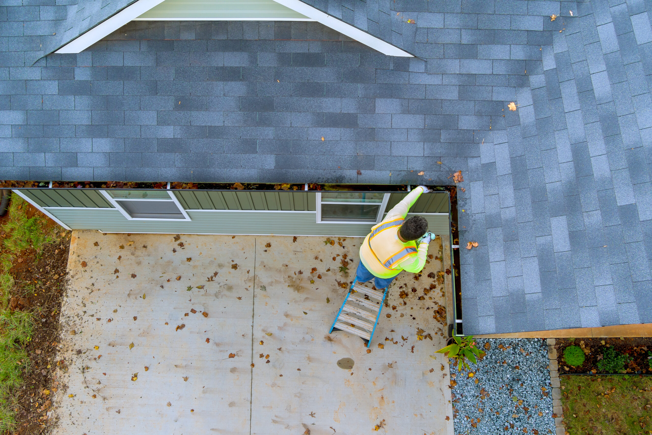 An employee is cleaning a clogged roof gutter drain with dirt, debris, fallen leaves