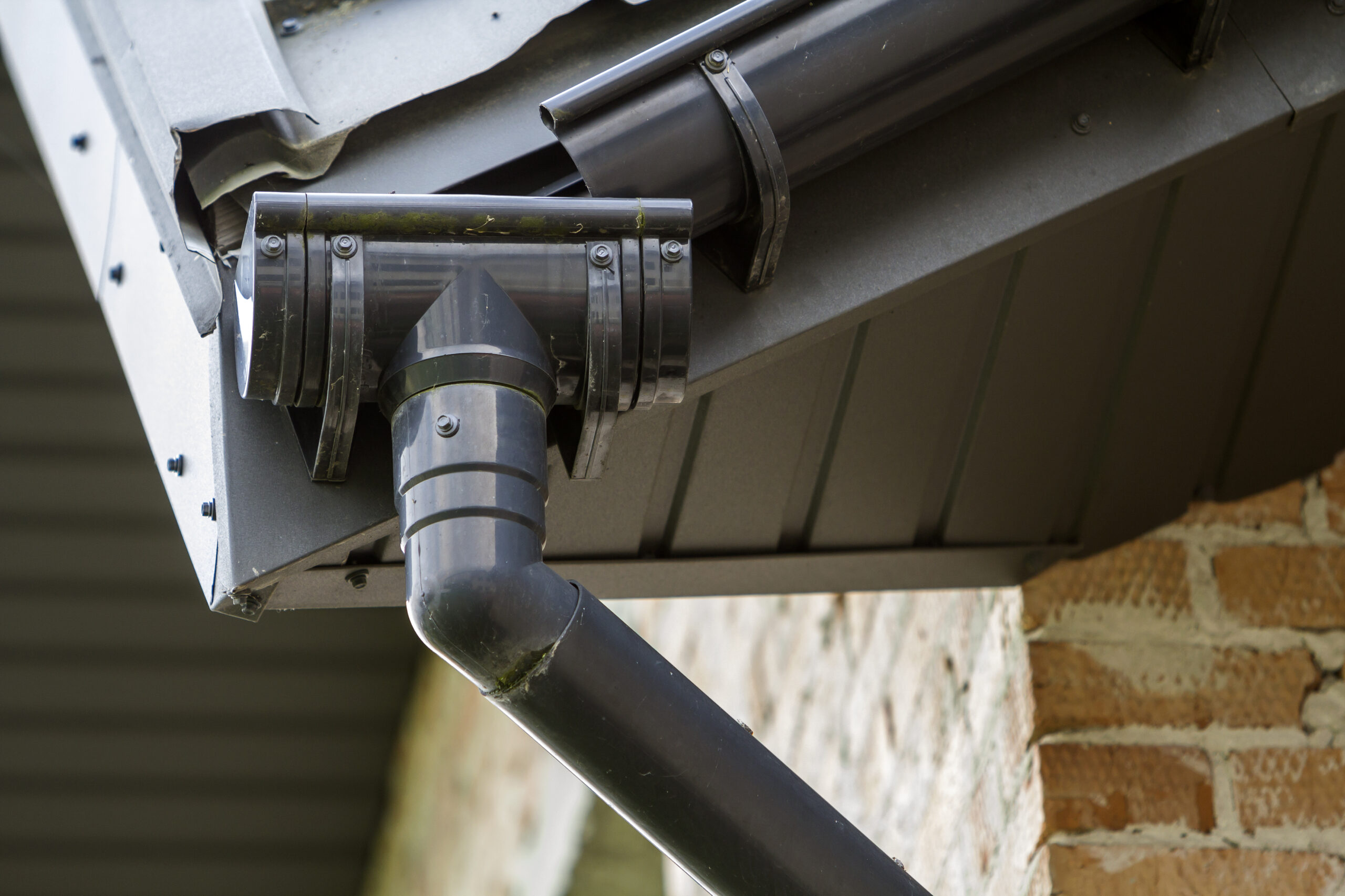 Close-up detail image of a corner of new built brick cottage house roof with steel gutter rain system. Professional construction and drainage pipes installation and connection concept.